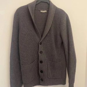 Grå stickad kofta från Guido Maria Kretschmer - Säljer en stilren grå stickad kofta från Guido Maria Kretschmer. Koftan har långa ärmar, knappar framtill och praktiska fickor. Perfekt för kyliga dagar! Pris är ej hugget i sten och är även öppen för byten