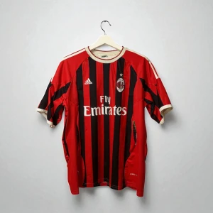 AC Milan Ibrahimovic matchtröja Adidas - Säljer en klassisk AC Milan fotbollströja från Adidas med Ibrahimovic och nummer 11 på ryggen. Tröjan är röd och svart med vertikala ränder, korta ärmar och vita detaljer. Officiell klubbmärke och Fly Emirates-tryck på bröstet. Perfekt för fans av Zlatan och Milan.