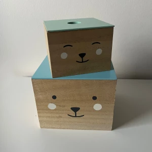 Söta förvaringslådor  - Två fyrkantiga förvaringslådor i trä. Locken är i pastellblått och mintgrönt med praktiskt hål för enkel öppning. Ungefärliga mått, stora lådan: 15cm bred, 15 cm djup och 12,5cm höjd. Lilla lådan: 11cm bred, 11cm djup och 8,5cm höjd.