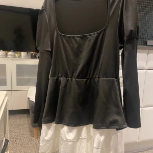 Svart långärmad peplumtop - Säljer en svart långärmad topp med fyrkantig ringning och peplumvolang nedtill. Toppen har lätt puffade axlar och är i ett mjukt, stretchigt material som känns skönt mot huden. Perfekt för dig som gillar en stilren men ändå trendig look.