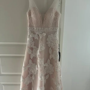 Rosa Klänning, Fest, Bröllop, Kväll, Storlek 8, Elegant, Söt - Superfin långklänning i champagne med djup v-ringning, dekorerad med pärlor i midjan och stora vita blommiga spetsapplikationer. Klänningen har en elegant och romantisk look med markerad midja och lätt utsvängd kjol.