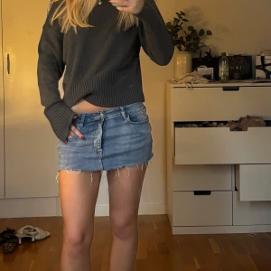 Blå lågmidjad jeanskjol med fransig kant - Säljer en snygg blå jeanskjol i klassisk modell med låg midja och fransig, rå kant nertill. Kjolen har fem fickor och stängs med knapp och dragkedja framtill. Perfekt för dig som gillar en avslappnad och trendig stil.