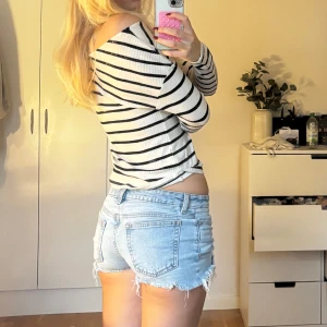 Ljusblå lågmidjade jeansshorts med fransad kant - Säljer ett par ljusblå jeansshorts med fransad kant och slitna detaljer. Gjort hålen själv och allt så finns inga andra som ser ut som dessa. De har låg midja, klassiska fickor både fram och bak samt knapp och dragkedja. Perfekta för varma dagar och en chill stil.