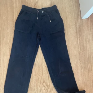 Svarta mjukisbyxor från Juicy Couture - Mysiga mörk blåa mjukisbyxor från Juicy Couture i mjuk fleece med dragsko i midjan, stora fickor fram och bakfickor med tryckknappar. Broderad JC-logga på ena fickan och guldfärgade detaljer. Perfekta för chill eller streetwear. Storlek 10/11. Säljer av inten andvändning och för korta. Använt typ 2-3 gånger.