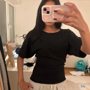 Svart topp med vida ärmar - En svart topp med rund halsringning och vida, korta ärmar. Sitter figurnära över midjan och har en enkel, stilren design som passar till mycket. Perfekt att matcha med både jeans och kjol. (Egen sydd)