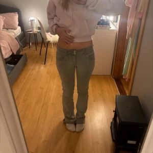 Grå bootcut jeans med låg midja - Säljer ett par gråa jeans med låg midja och bootcut-snitt. Jeansen har klassisk femficksdesign, dragkedja och knapp framtill. Snygg passform som sitter tajt upptill och släpper ut vid benen. Perfekta för dig som gillar en clean och enkel look.