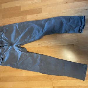 Grå jeansbyxor från SHEASE W34 L34 - Snygga grå jeansbyxor från SHEASE by Stock & Honk i klassisk femficksmodell. Byxorna har rak passform och är tillverkade i bomullsmix med dragkedjegylf. Perfekta för dig som gillar stilrena och enkla jeans.