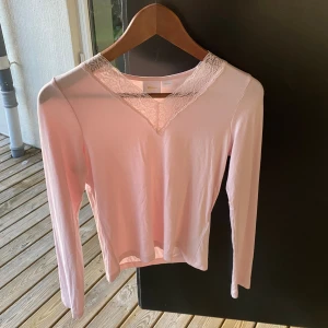 Ljusrosa långärmad topp med spets Gina Tricot - Supersöt ljusrosa långärmad topp från Gina Tricot med v-ringning och fina spetsdetaljer runt halsen. Mjuk och skön, perfekt att styla med jeans eller kjol. Enkel men ändå med en touch av romantisk vibe.