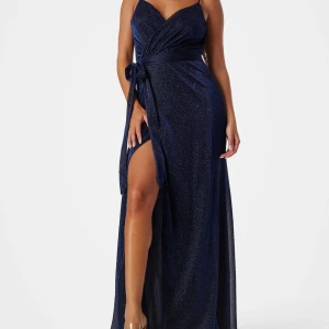 Marinblå glittrig långklänning omlott - Snygg marinblå långklänning med glittrigt tyg, omlottmodell och v-ringning. Klänningen har smala axelband, markerad midja med knyt i sidan och en hög slits framtill som ger en extra touch.
