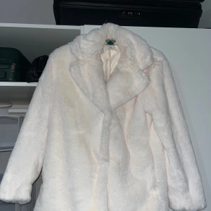 Vit pälsjacka  - Supermjuk och fluffig vit pälsjacka med bred krage och lång ärm. Jackan har en klassisk rak passform och är perfekt för att hålla värmen under kyliga dagar. Snygg att styla till både jeans och kjol för en trendig look.