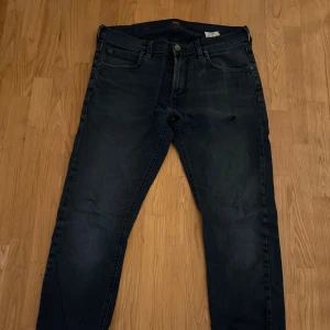 Mörkblå Lee ”Luke” jeans straight fit - Snygga mörkblå jeans från Lee med klassisk femficksdesign och raka ben. Jeansen har Lee-logga på bakfickan och svart patch bak i midjan. Tillverkade i mjukt denimtyg som ger en skön känsla och stilren look.