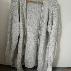 Ljusgrå stickad kofta från H&M L.O.G.G. - Mysig och oversized ljusgrå stickad kofta från H&M L.O.G.G. Koftan är öppen framtill, har långa ärmar och ribbade detaljer på axlar och muddar. Perfekt att slänga på sig när det är kyligt ute.