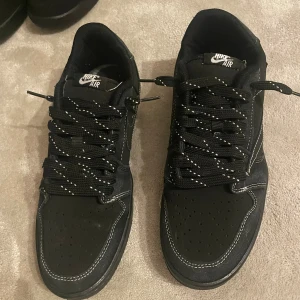 Nike Air Jordan 1 retro Low OG travis scott black phantom  - Svarta Nike Air Jordan 1 retro Low OG SP Travis scott black phantom (PS) med vita kontrastsömmar och broderade detaljer på hälen. Skorna har perforerad tå, svart sula och svarta skosnören med vita prickar. Tillverkade i skinn och syntetmaterial, med klassisk Air Jordan-logga och bi-detalj bak.