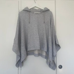 Grå poncho-hoodie från Esprit - Superfin grå hoodie från Esprit i ponchostil med huva och snörning. Oversized fit med vida ärmar och känguruficka framtill. Perfekt för hösten! Gjord i mjuk bomullsblandning.