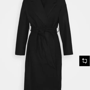 Svart omlottkappa med bälte - Stilren svart kappa med omlottknäppning och bälte i midjan. Jackan har klassisk krage, raka långa ärmar och en rak passform som ger en clean look. Perfekt för dig som gillar minimalistisk stil och vill ha en tidlös jacka i garderoben. ORDINARIE PRIS: 629