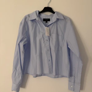 Ljusblå skjorta från Banana Republic - Snygg ljusblå skjorta från Banana Republic i klassisk modell med krage, bröstficka och knappar framtill. Skjortan är långärmad och har en rak, något croppad passform. Nypris: 65 USD