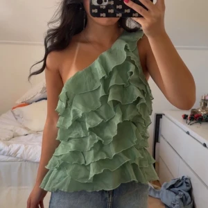 Grön volangig oneshoulder topp  - Supersöt grön oneshoulder topp med volanger i storlek (34), passar ngn med S perfekt 💗Dragkedjan kan vara lite trög, men annars inga defekter! 