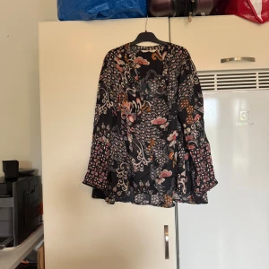 Odd molly blus  - Säljer en otroligt vacker Odd Molly blus i en svart bottenfärg med yr blommigt och detaljerat mönster i massor av färger som bland annat, orange, beige och olika nyanser av rosa. Storlek 1 som enligt deras storleksguide motsvarar en storlek S. Men det kan vara något rymligare. Mycket fint skick, jag hittar inga synliga anmärkningar eller defekter. 
