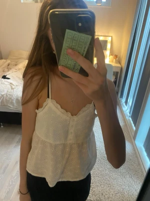 Vit broderad linnetopp från H&M - Säljer en söt vit linnetopp från H&M med tunna axelband och broderade blommor. Toppen har gulliga knappar framtill och en vågig spetskant längs halsringningen. Perfekt för sommaren eller även till en snygg kofta. Har endast använt fåtal gånger!