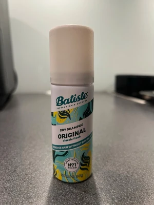 Batiste Original Dry Shampoo 50ml - Batiste Original Classic Fresh torrschampo i en smidig 50ml sprayflaska med vit kork och färgglad design i turkos, gul och svart. Ger håret en fräsch känsla med klassisk doft och passar perfekt för att snabbt fräscha upp håret mellan tvättar. Enkel att använda och lätt att ta med i väskan.
