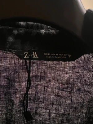Svart omlottblus från Zara - Säljer en svart omlottblus från Zara i storlek XL. Blusen är tillverkad i ett tunt och luftigt linnematerial, har långa ärmar och knyt framtill.  Aldrig använd 