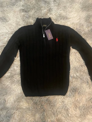 Svart stickad Polo Ralph Lauren - Svart stickad tröja från Polo Ralph Lauren. Tröjan är väldigt bekväm och har skönt material. Perfekt för dig som gillar klassisk stil med en modern touch.Tröjan är i storlek S och passar även M