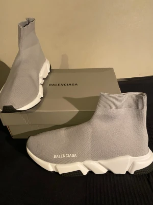 Balenciaga Speed Grå - Säljer ett par Balenciaga Speed Trainer sneakers i ljusgrå färg med vit och svart chunky sula. Skorna har en strumpliknande, stickad ovandel i syntetmaterial och Balenciaga-logga på sidan och hälen. Modern och clean design som är riktigt populär just nu.