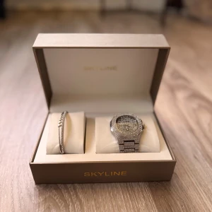 Ingen väst på bilderna - Bilderna visar ett Skyline smyckeset med klocka och armband i silverfärg, dekorerade med glittrande stenar, i en lyxig ask. Mycket blingig klocka om man gillar att sticka ut. Får med länkar ifall de är för litet!