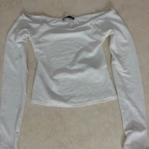 Vit glittrig offshoulder topp  - Säljer en vit offshoulder topp i storlek S. Toppen har långa ärmar och är täckt av glittriga detaljer som ger en snygg och festlig vibe. Endast testad. Perfekt nu till nyår eller fester! Ordinarie pris 159kr
