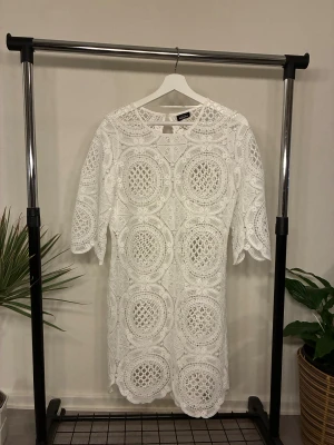 Vit spetsklänning - Säljer en vit kortklänning från Kappahl med unikt cirkulärt spetsmönster och halvärmar. Klänningen har rund hals och pärlknappar i nacken. Materialet är spets med vackra detaljer som ger en lyxig känsla. Passar både  S/M 