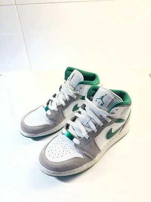 Nike Air Jordan 1 Mid vit/grön/grå - Sparsamt använda, ca 10 gånger. Säljer pga används ej. Kartong finns tyvärr inte kvar. Köpta 2022, nypris då ca 6000 kr. 