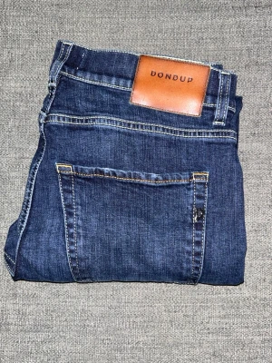Mörkblå Dondup jeans - Snygga mörkblå jeans från Dondup med klassisk femficksdesign och kontrastsömmar. Jeansen har en regular passform och är tillverkade i mjukt denimtyg med en skön känsla. Perfekt för dig som gillar stilrena och tidlösa jeans. Hör av er vid intresse/ frågor!