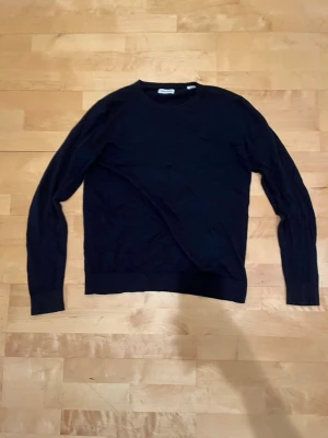 Mörkblå tröja från Jack & Jones - Snygg mörkblå långärmad tröja från Jack & Jones i storlek M. Tröjan har en klassisk rund hals och är tillverkad i mjuk bomull, perfekt för chill dagar eller när du vill ha en enkel stil. Passformen är normal och den funkar lika bra till jeans som till chinos.