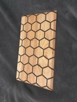 Skärbräda  med hexagonmönster och epoxy -  med ett coolt hexagonmönster på ena sidan. Brädan är i ljust trä och har svarta linjer som bildar ett bikakemönster. Perfekt som dekoration eller serveringsbräda och skärbräda man kan använda den till allt.