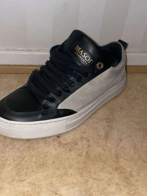 Svarta och beige sneakers från Masot garments - Säljer ett par stilrena sneakers från Masot Garments i svart och beige. Skorna har svart skinn framtill och detaljer i mocka på sidorna, samt vita tjocka sulor. Svarta snören och gulddetalj vid snörningen ger en exklusiv vibe.