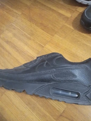 Svarta Nike Air Max sneakers - Säljer ett par svarta Nike Air Max sneakers med klassisk synlig luftbubbla i sulan. Skorna har en rund tå och är tillverkade i skinn med snygga detaljer och texturer på ovandelen. Perfekt för dig som gillar stilrena och sportiga sneakers.