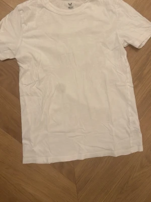 Vit t-shirt från SOC - En klassisk vit t-shirt från SOC i storlek 158-164. T-shirten har rund hals och korta ärmar, tillverkad i mjuk bomull som känns skön mot huden. Perfekt för dig som gillar enkel och clean stil.