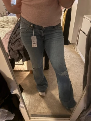 Blå bootcut jeans med slitningar - Snygga blå jeans med bootcut-snitt och slitna detaljer vid knäna. Perfekta för dig som gillar en avslappnad och trendig look. Lappen har tagits av men aldrig använda. Pris går att diskuteras 