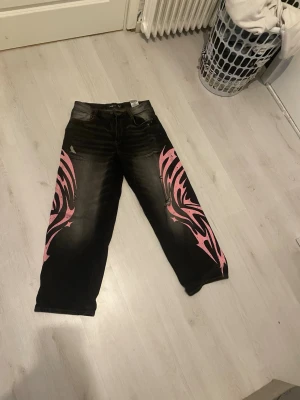 BAGGY jeans med rosa tribal från fbsister - Unika svarta jeans från FBSister i storlek L med fett rosa tribal-mönster längs båda benen.🎀BAGGY!