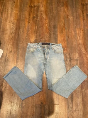 Ljusblå jeans från Jacob Cohën - Säljer ett par ljusblå jeans från Jacob Cohën med klassisk femficksdesign och orangea kontrastsömmar. Jeansen har rak passform och knappgylf med snygga detaljer på insidan. Materialet är mjukt denim och det finns en broderad logga på fickan. Modell Style 688.
