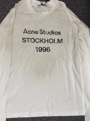 Vit långärmad t-shirt Acne Studios S - Vit långärmad t-shirt från Acne Studios med tryck 'Acne Studios STOCKHOLM 1996' på bröstet. Tillverkad i 100% bomull och har en klassisk rund hals. Perfekt för dig som gillar stilrena och ikoniska plagg med enkel design.
