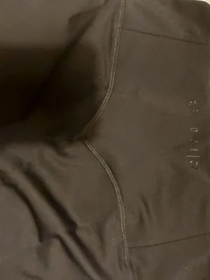 Svarta leggings från Relode - Säljer ett par svarta leggings från Relode med hög midja och snygga sömmar som ger en schysst passform. Materialet är stretchigt och mjukt, perfekt för träning eller chill. Diskret logga på benet. Passar dig som gillar stilrena och bekväma träningskläder.