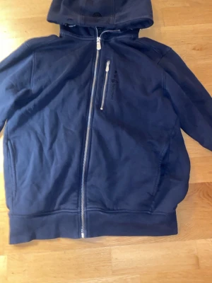 Sail racing hoodie - En marin blå sail racing hoodie som är lite fåtal ställen där man ser slitningar men den är fortfarande i ett bra skick och har några år kvar att ge. Den är i storlek m 