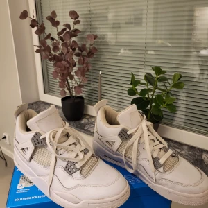 Nike Air Jordan 4 IV Retro Pure Money Vit 42 - Säljer ett par Nike Air Jordan 4 Retro i helvitt skinn med grå detaljer och klassisk mesh på sidorna. Skorna har snörning, rund tå och ikonisk Jumpman-logga på hälen. Perfekta för dig som gillar stilrena och tidlösa sneakers med streetkänsla.