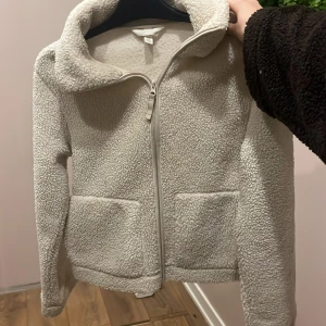 Vit teddyjacka med dragkedja XS - Mysig vit teddyjacka i storlek XS med fluffig yta och två stora fickor framtill. Jackan har hög krage och hel dragkedja, super mysig och går och använda i alla årtider 