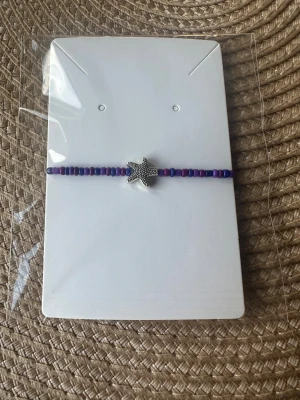 Lila pärlarmband med sjöstjärna - Snyggt hemmagjort armband med små lila och blå pärlor och en silverfärgad sjöstjärna i mitten. Perfekt accessoar för dig som gillar havsinspirerade detaljer och färgglada smycken. Armbandet är enkelt och passar till många olika stilar.