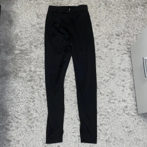 Svarta kostymbyxor från SHEIN XS - Svarta kostymbyxor från SHEIN i storlek XS. Byxorna har en smal passform, midwaist och är tillverkade i ett mjukt syntetmaterial. De har en enkel knapp framtill och raka ben. Perfekta för en clean och stilren look.