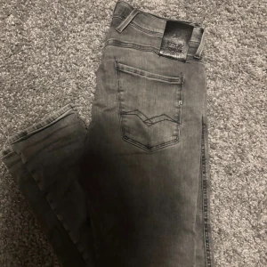 Replay Anbass grå jeans, storlek 31/32 - Snygga Replay Anbass jeans i en tvättad grå färg med klassisk femficksdesign, mycket bra skick men tyvärr har det blivit ett litet hål vid skrevet som ni kan se på sista bilden men inget som syns vid användning, hör av er vid frågor🤩