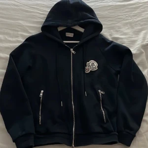 Svart hoodiejacka från Moncler - Mörkblå Moncler zip hoddie med dubbel logga, Storlek M men skulle säga att den nog är lite liten i storlek då jag är 180cm och tycker den känns lite kort i armarna. Knappt använd sen jag köpte den därav säljer jag. Inga skador eller fläckar så den är i mycket bra skick! QR kod fungerar, kan skicka fler bilder vid intresse 