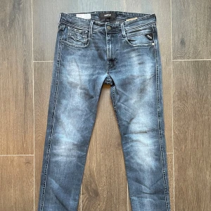 Replay Anbass slim fit jeans blå - Snygga Replay Anbass jeans i tvättad blå färg med slim fit-passform. Modell är blue jeans med diskreta slitningar och läderpatch med Replay-logo bak. Jeansen har raka ben och är tillverkade i mjukt denimtyg för en bekväm känsla. Det är bara att skriva om funderingar eller prisdiskutering 🙃